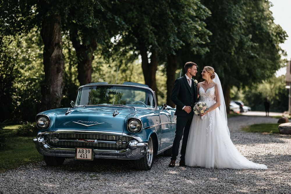 Vintage blue classic car parked on tree-lined path serves as elegant backdrop for wedding photography session.