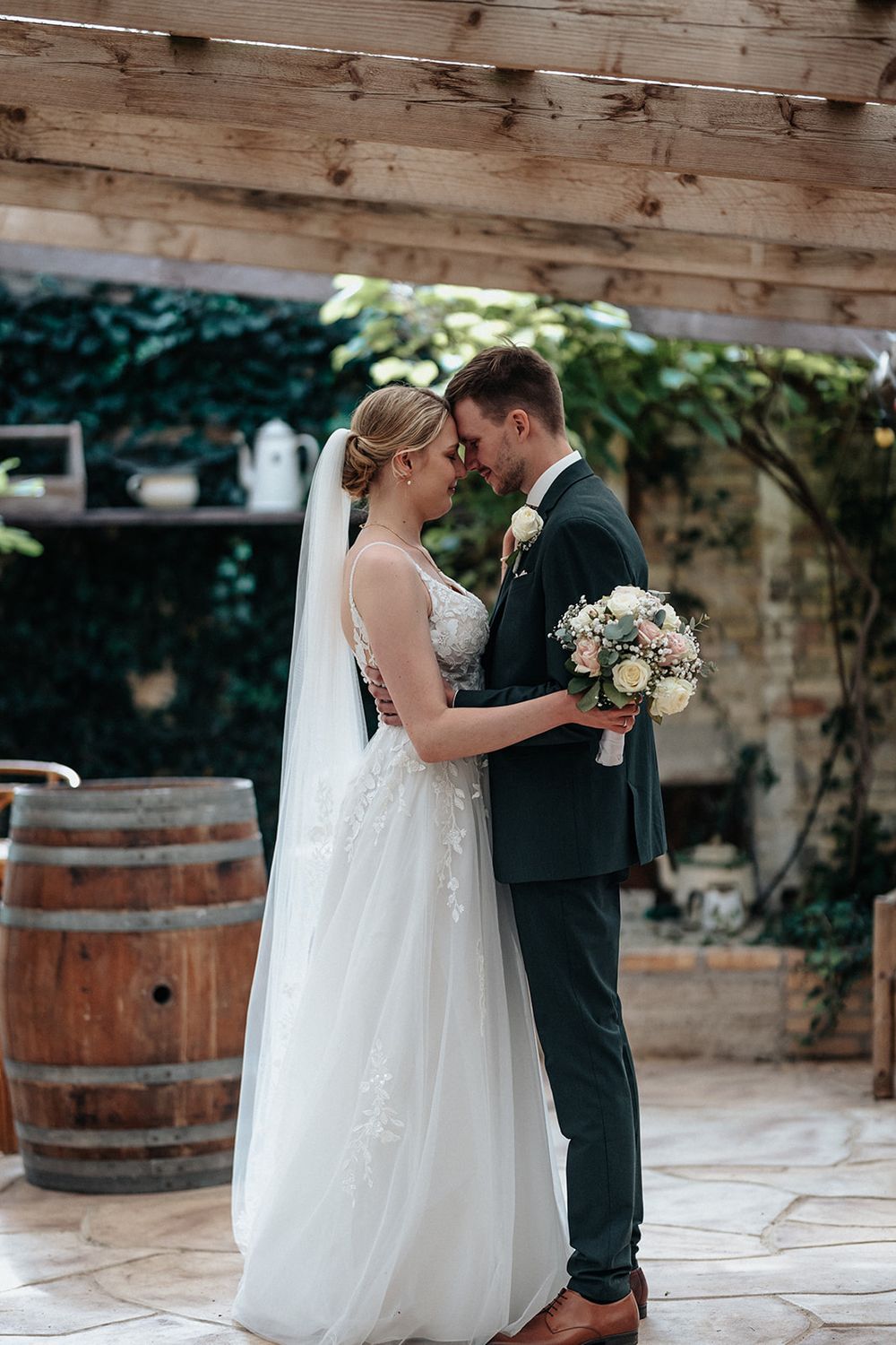 A romantic wedding couple shares intimate moments in a rustic venue with wooden barrels and stone walls.