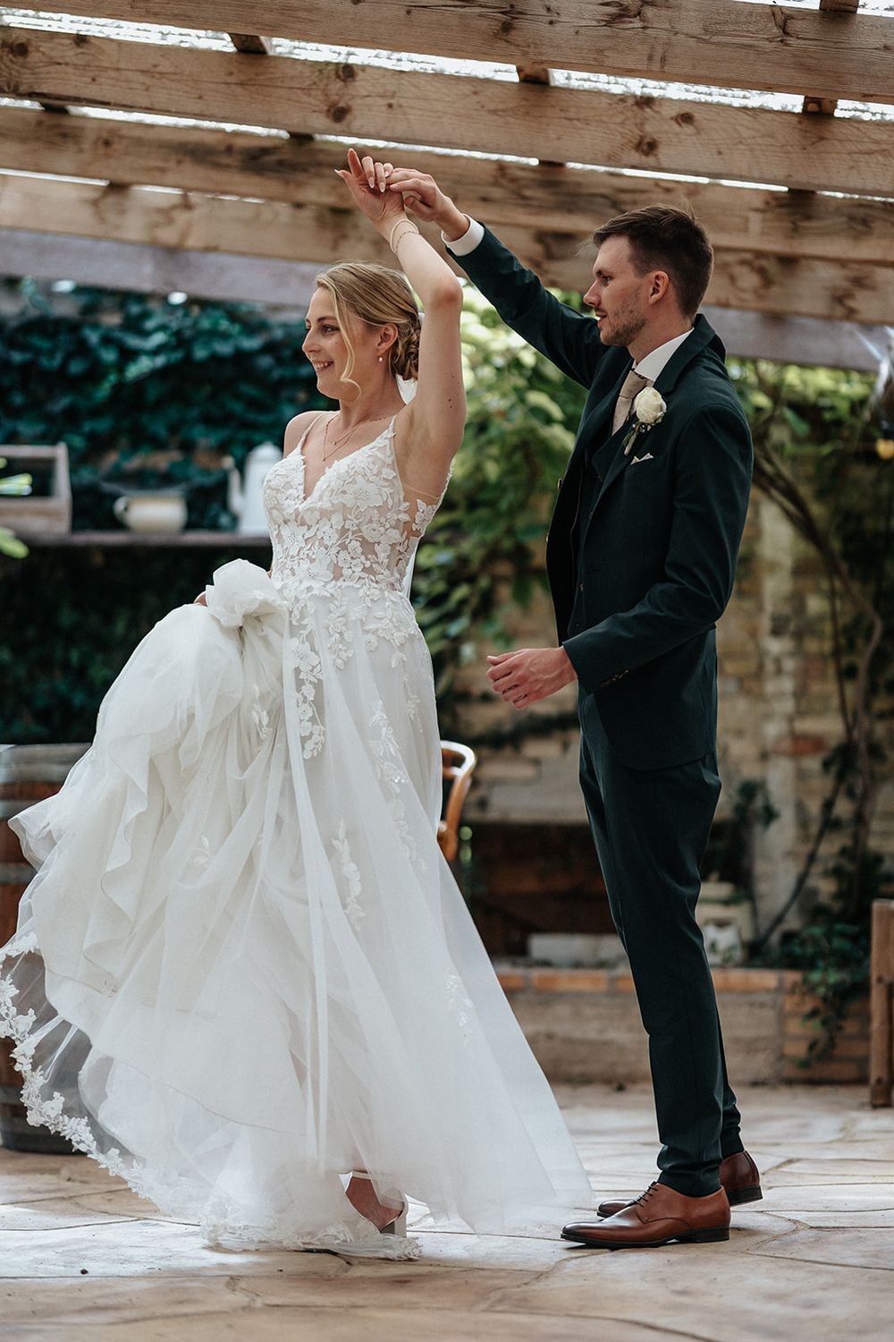 A couple dancing at their wedding, with the bride's white lace dress flowing gracefully as they twirl on a wooden floor.