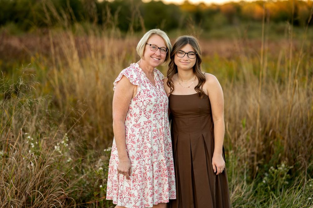Mother and daughter smiling together in a field at golden hour sunset.