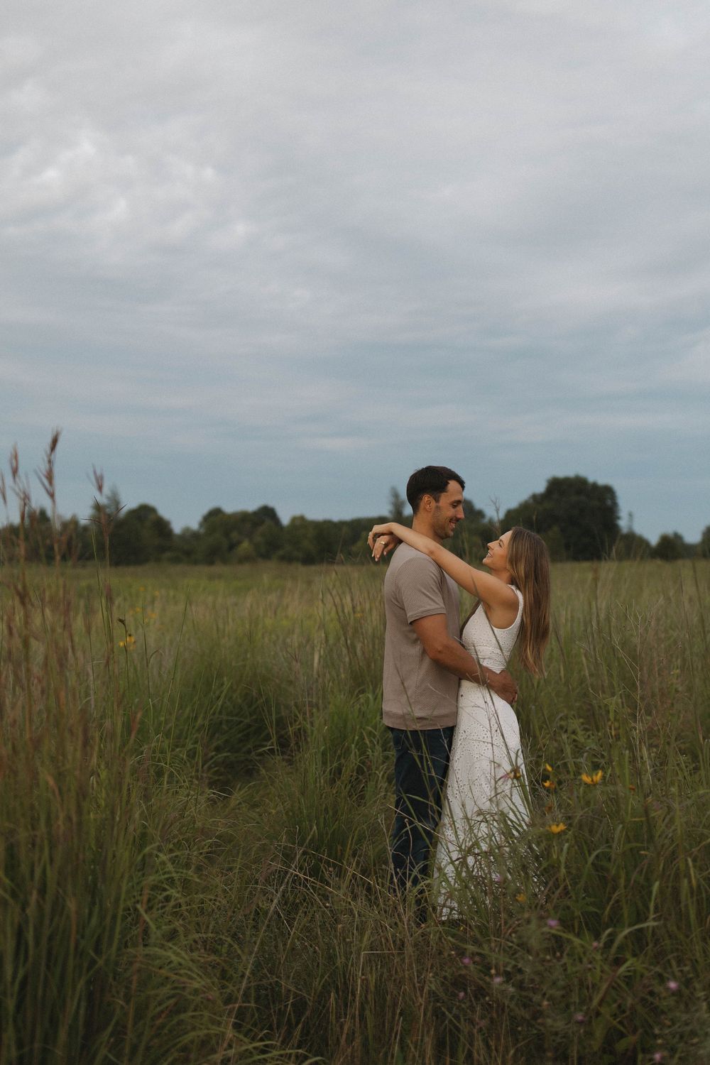 Couple dancing in a tall grass field under cloudy skies.