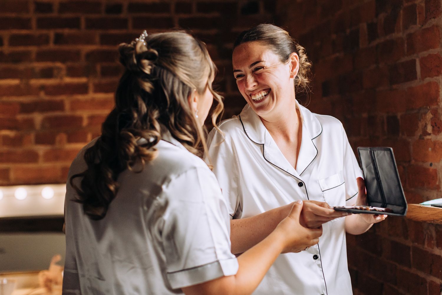 Two people in matching white outfits share a laugh in front of exposed brick walls.