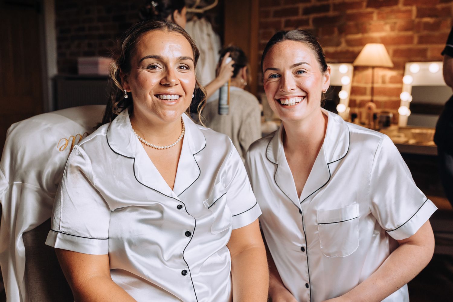 Two people in matching white pajama sets share a candid moment against exposed brick walls.