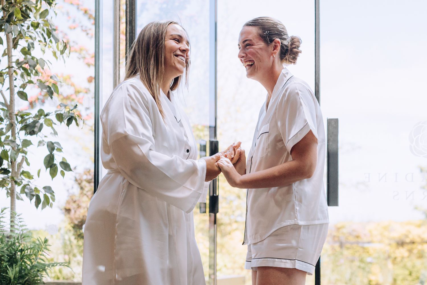 Two people in white shirts share laughter near bright windows.