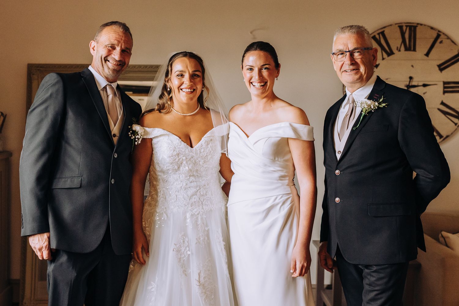 Wedding party members in formal attire pose together against a neutral wall with a clock.