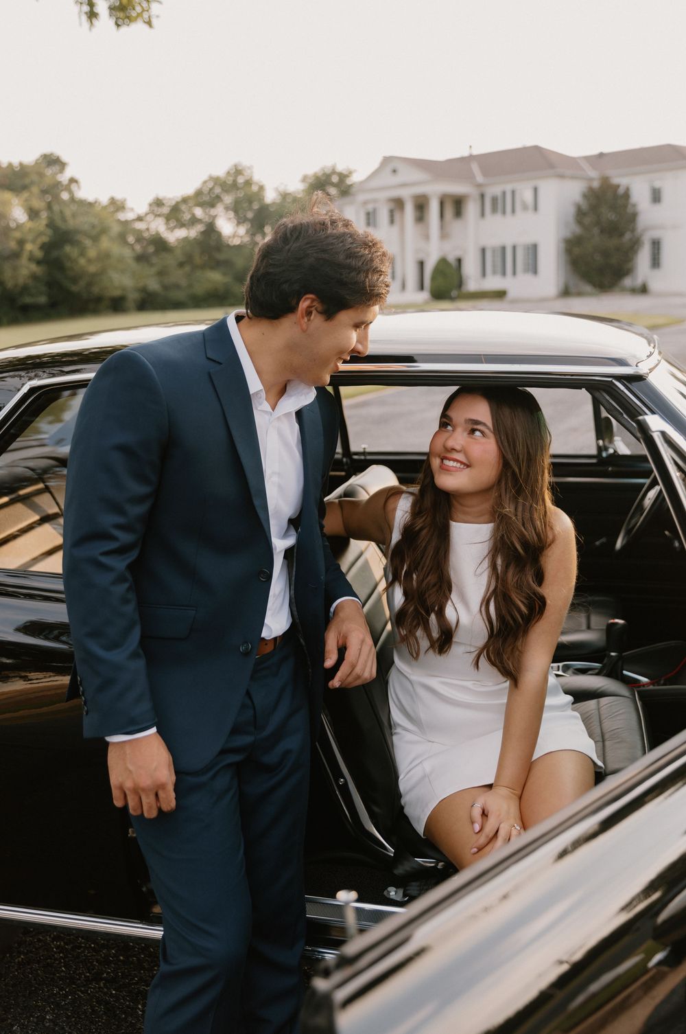 Romantic moment captured near a classic black car with elegant formal attire.
