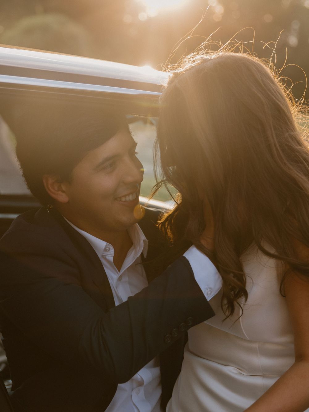 Romantic couple sharing an intimate moment in a car with golden sunlight streaming through the windows.