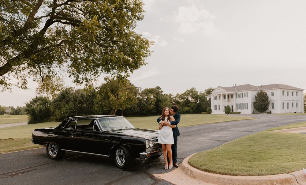 A classic black vintage car parked in front of a stately white mansion during an outdoor event.