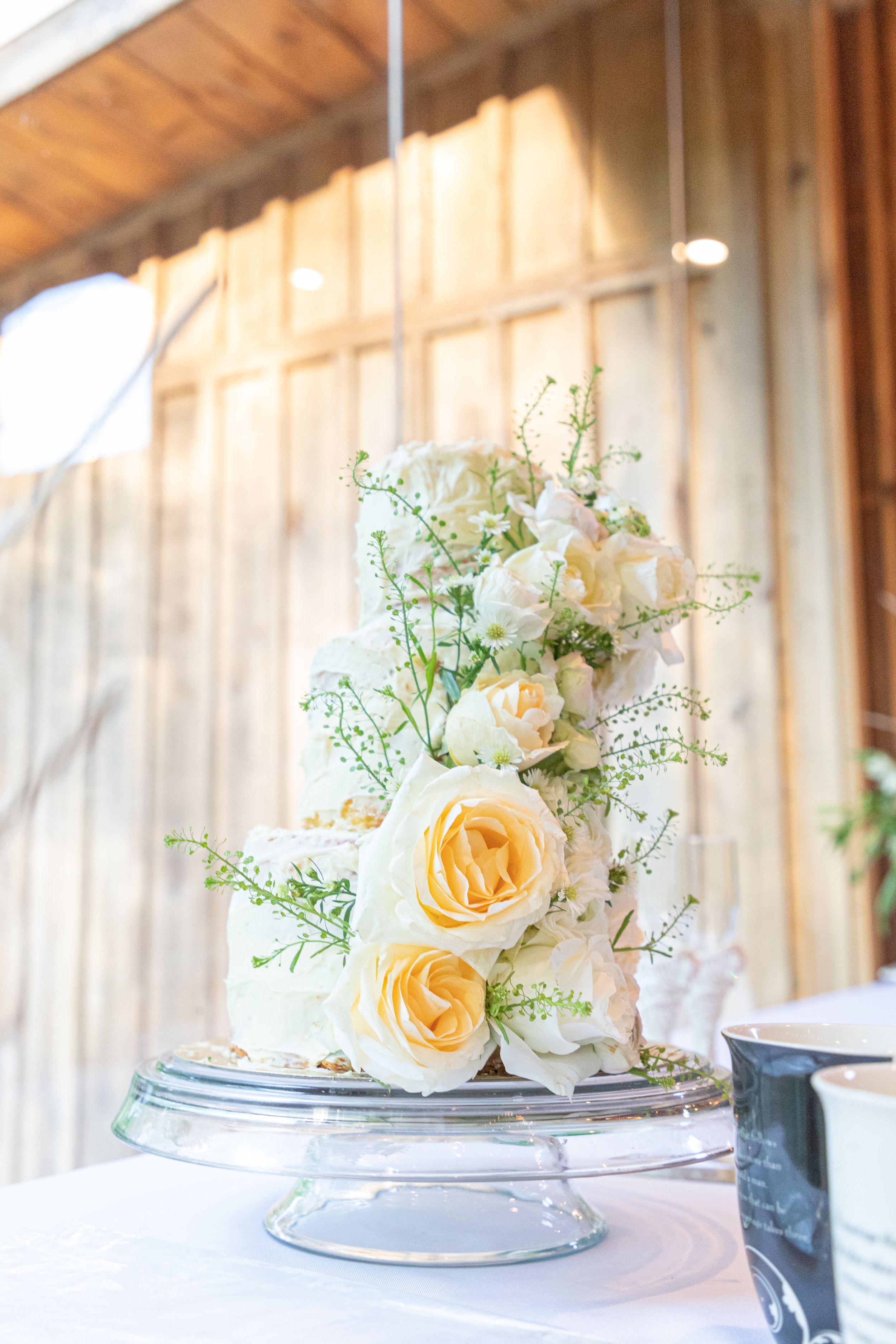 Elegant white and yellow roses decorate a tiered wedding cake on a silver cake stand.