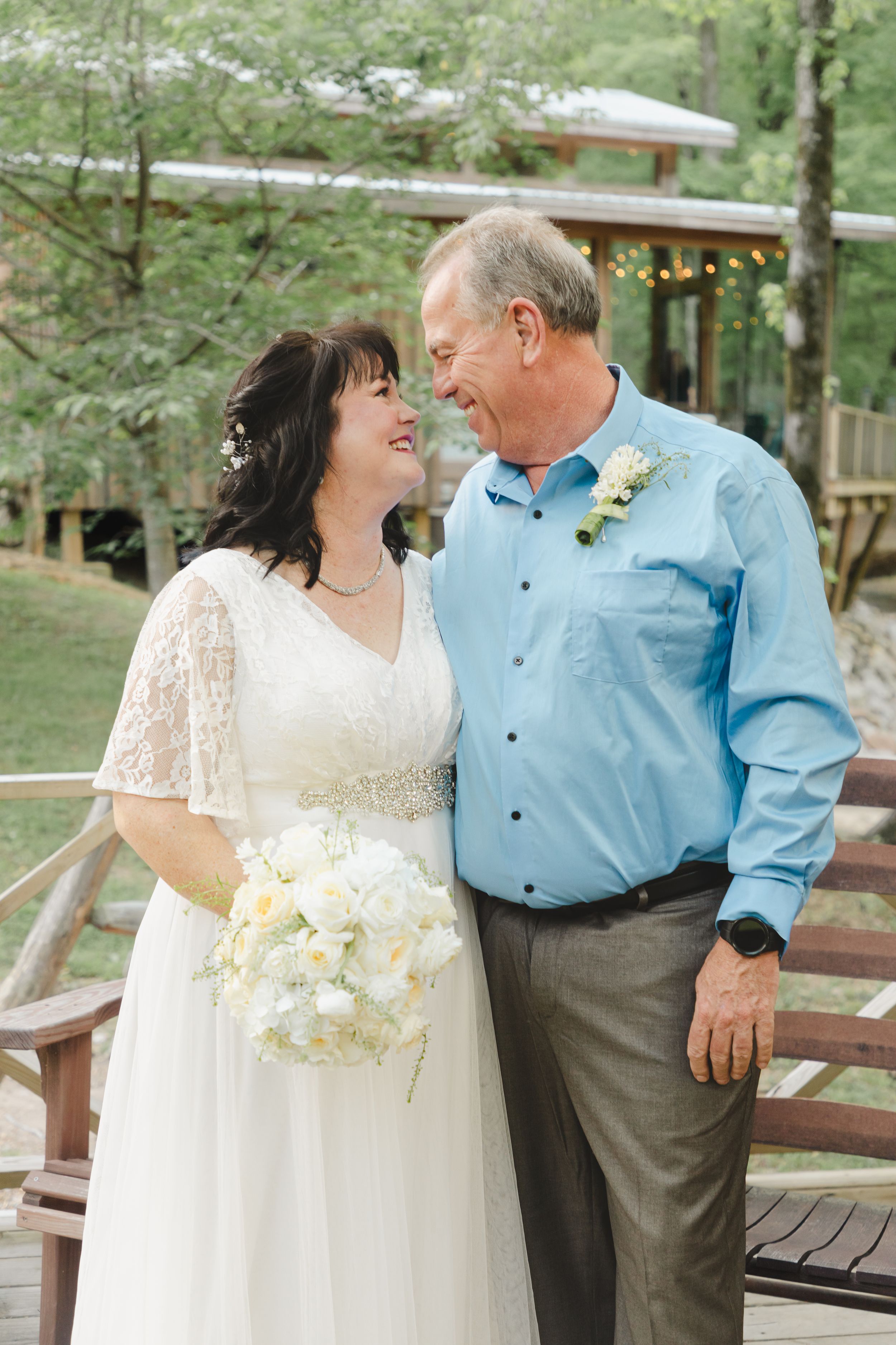 A joyful wedding couple sharing a tender moment outdoors on a wooden deck.