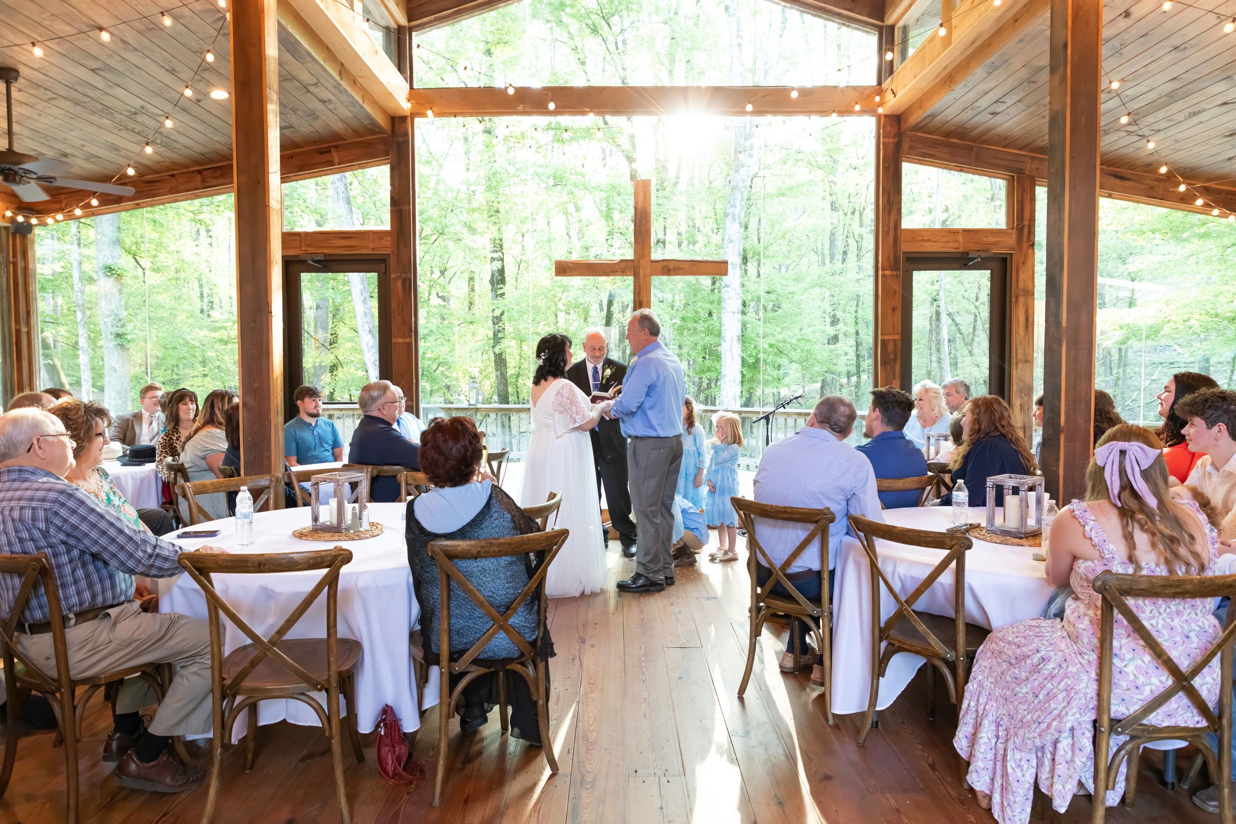 Wedding reception in a rustic wooden chapel with guests seated at tables and string lights overhead.