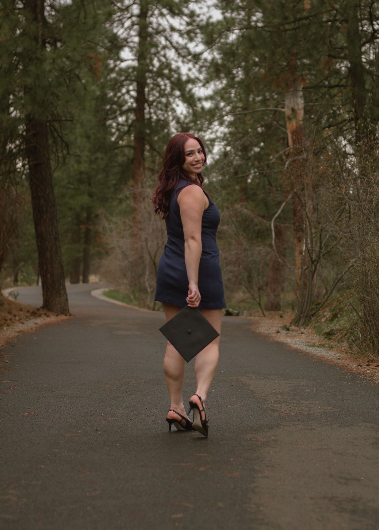 Redheaded woman in navy attire holding graduation cap for portraits to use on grad announcements for Gonzaga College in Spokane, WA.