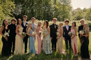 Large group of prom-dressed teens posing outdoors, wearing colorful gowns and suits in a lush green setting.
