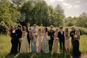 Group of elegantly dressed teens pose together in green field celebrating prom day.