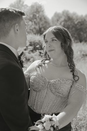 Black and white photo of a bride in a beaded strapless gown gazing at her groom during an outdoor wedding ceremony.