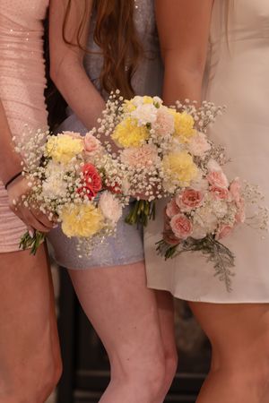 Bridesmaids in pink dresses holding colorful bouquets of yellow carnations, pink roses, and baby's breath flowers.