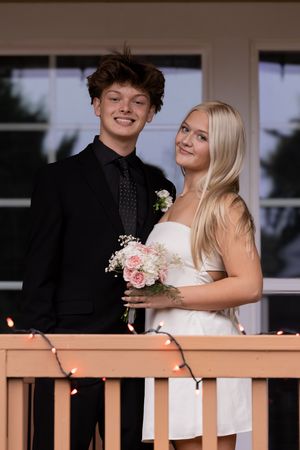 Young couple in formal attire share romantic moments on a porch decorated with string lights.