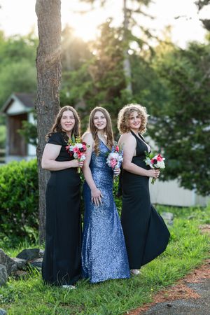 Three bridesmaids in black and blue dresses pose together outdoors during a wedding photoshoot.
