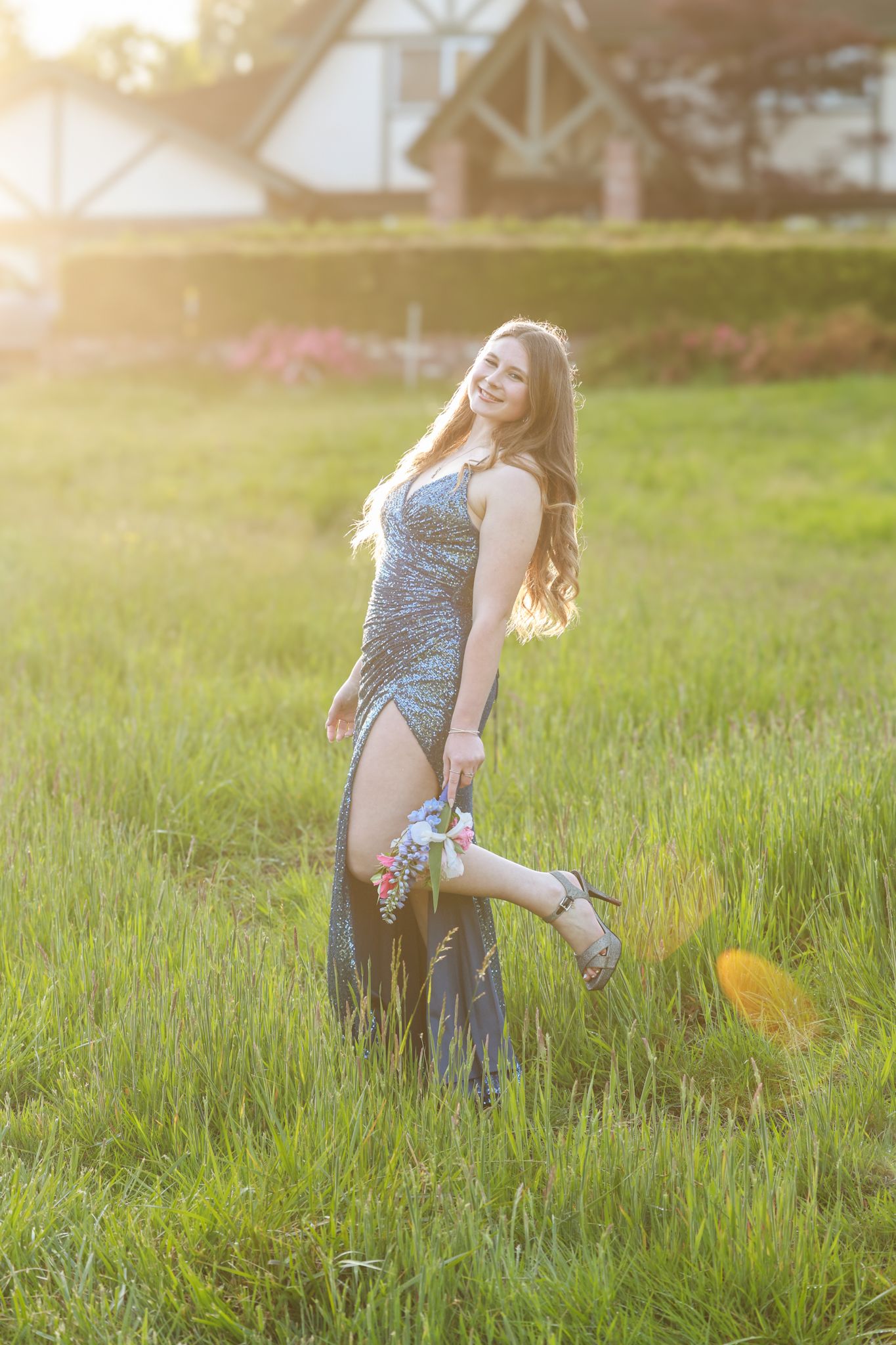 A person in a floral dress dances playfully in a sunlit grassy field during golden hour.