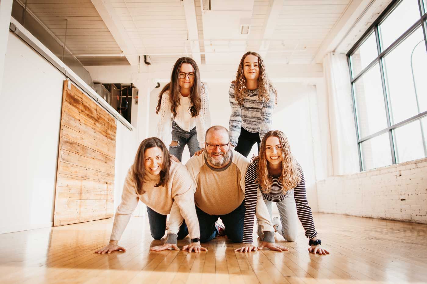 Group of people forming a creative human pyramid pose on wooden floor in bright modern space with windows.