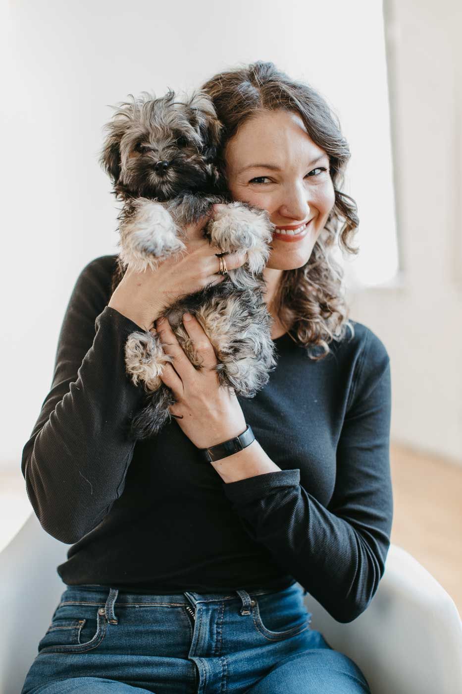 A joyful moment captured with someone holding a small fluffy dog while wearing a black sweater and jeans.