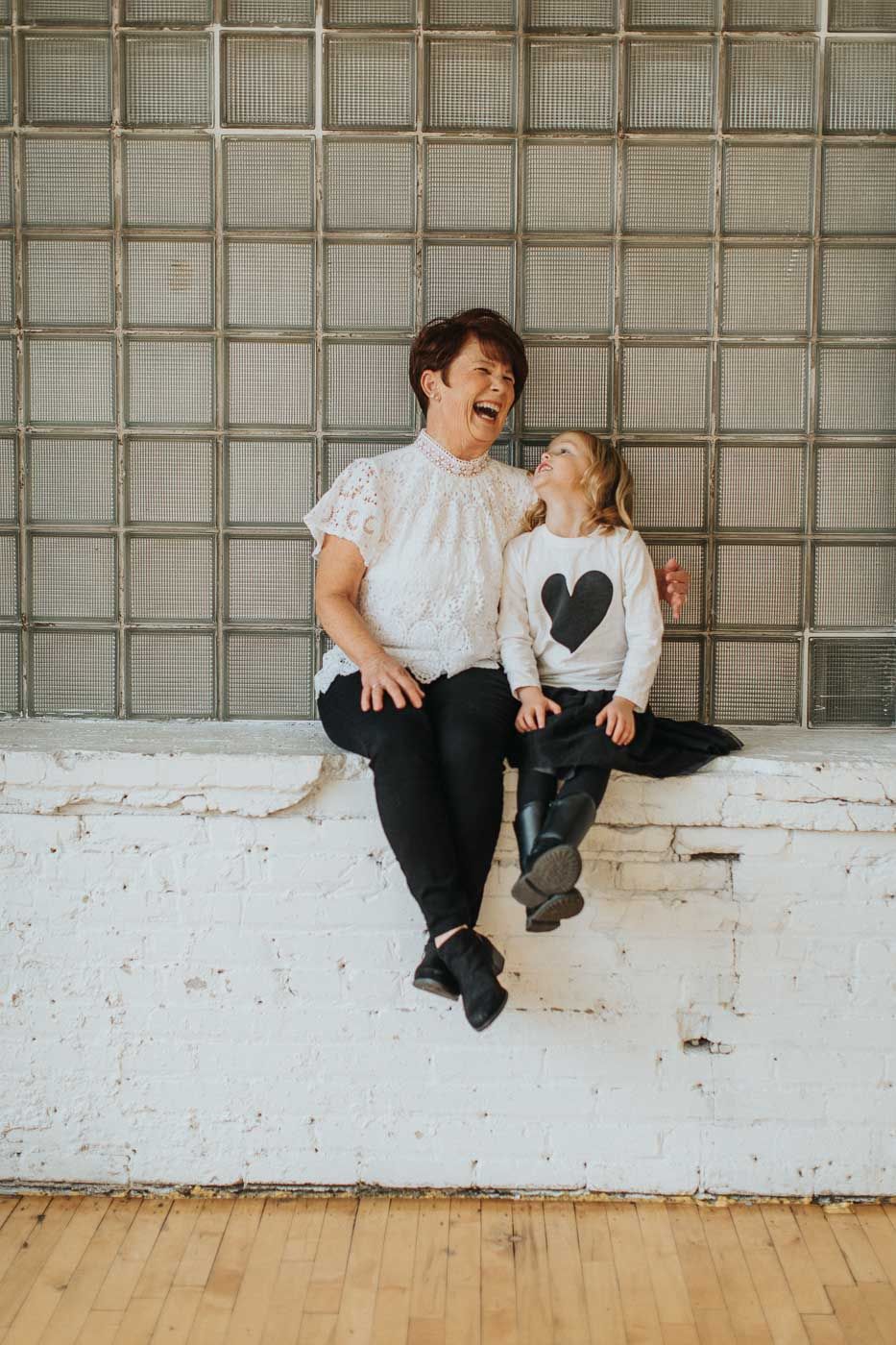 Two people sit and share a laugh together against a textured wall background.