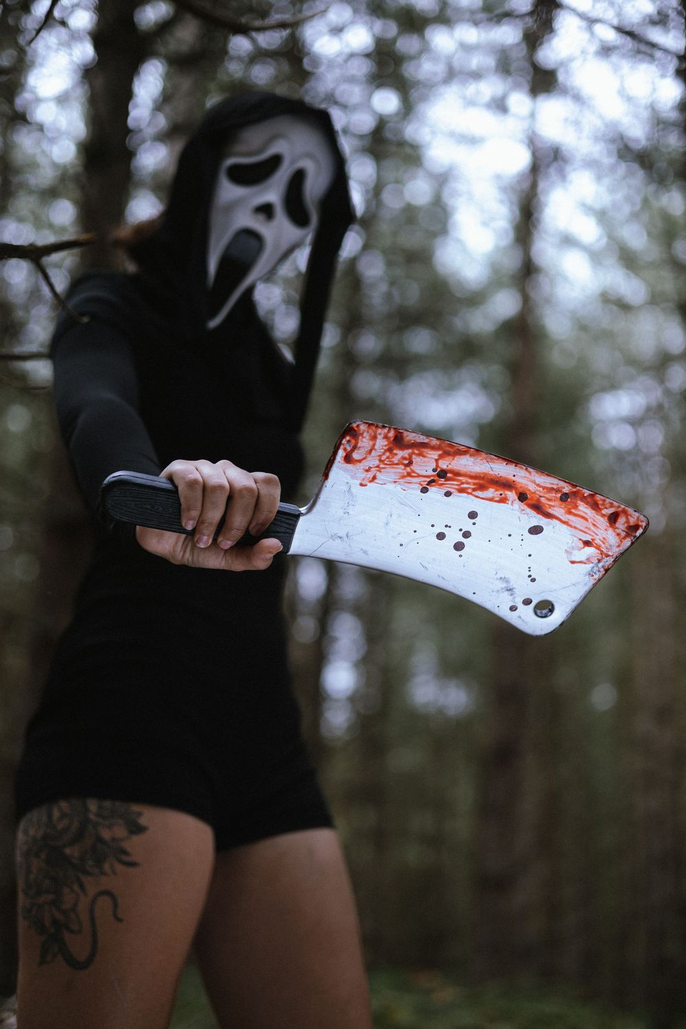 A person in a ghost mask holds a bloody cleaver in a dark forest setting, creating a spooky Halloween-like scene.