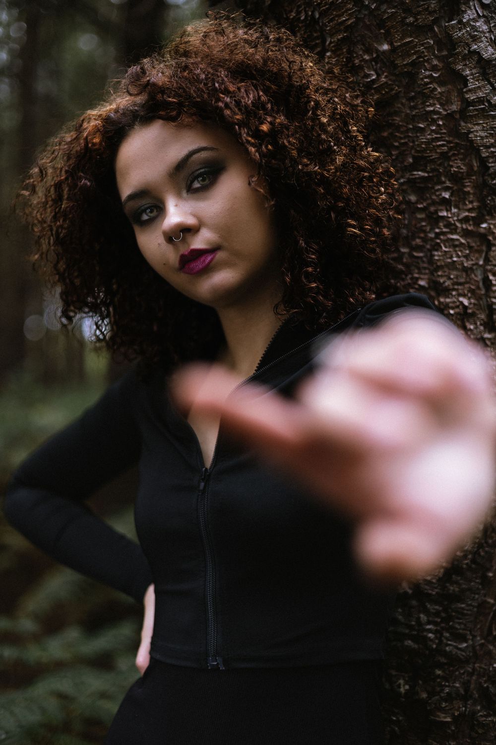 A series of moody forest portraits showing someone with curly hair wearing black and red lipstick in dramatic poses.