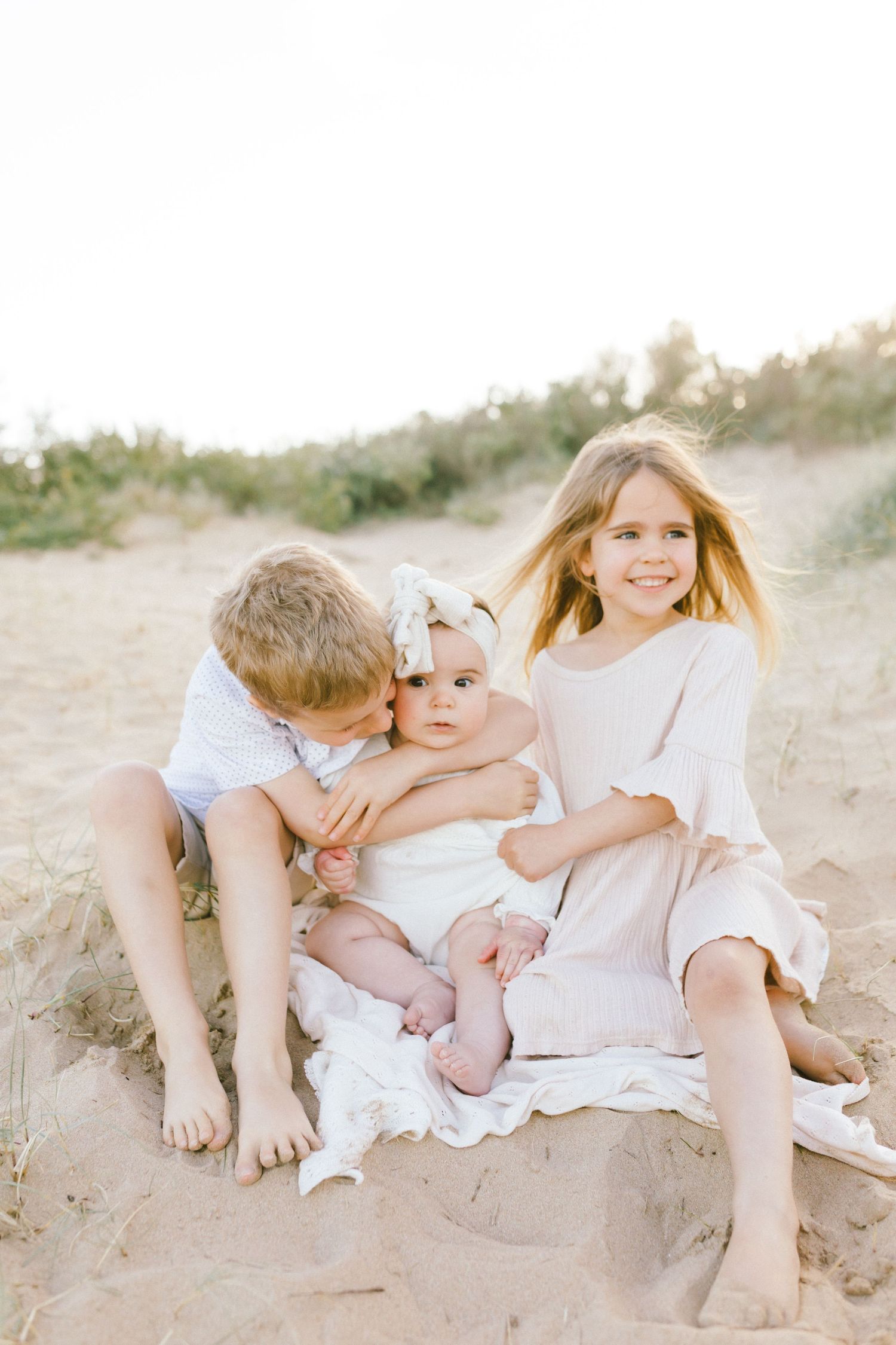 Children in white clothing play together on a sandy beach during golden hour.