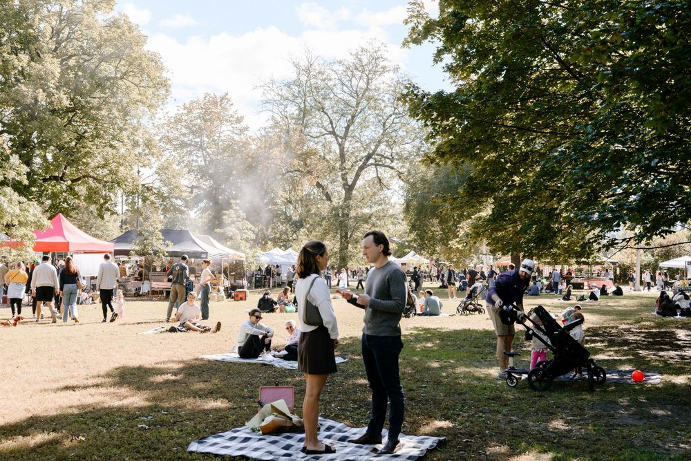 People enjoying a sunny autumn day in a park with blankets spread out on the grass for picnicking and relaxation.