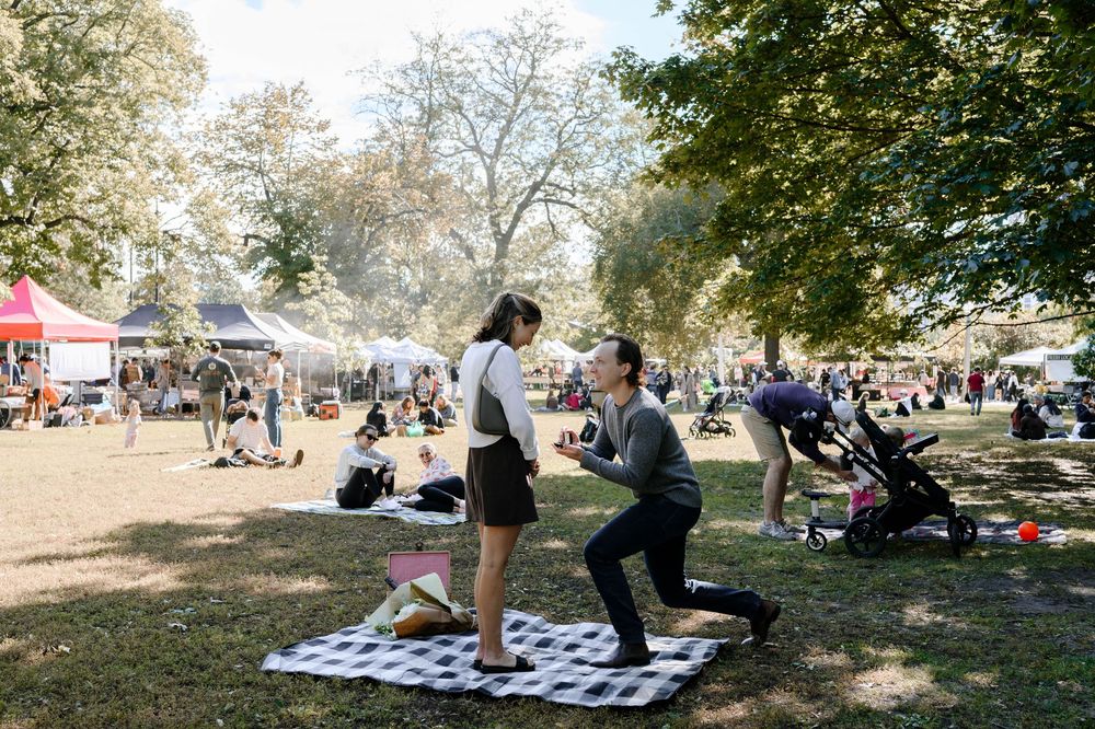 People gather in a park for outdoor activities with blankets spread on grass under autumn trees.