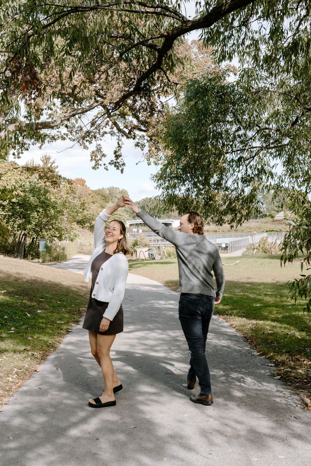 A couple dancing and twirling on a paved path surrounded by autumn trees.