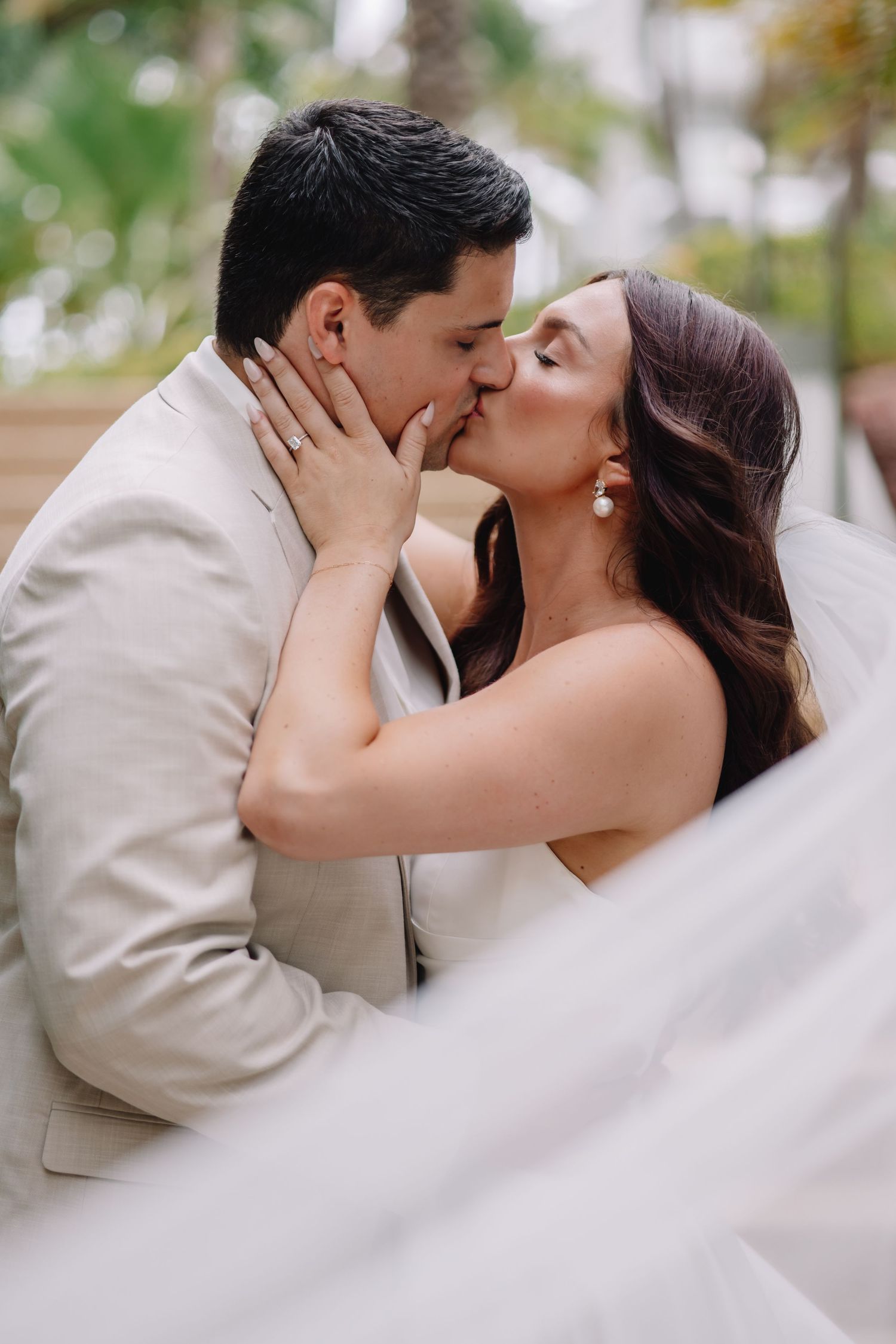 Romantic wedding kiss captured through flowing veil in outdoor setting.