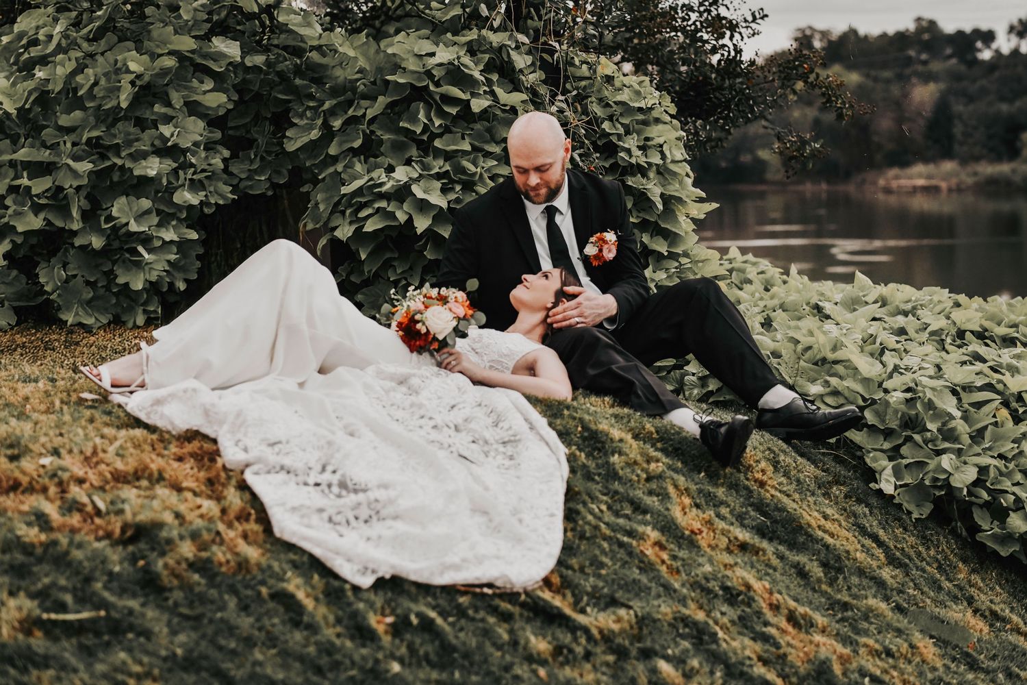 a bride lays in the lap of her groom on a hill next to the rivers edge at the venue at tin top