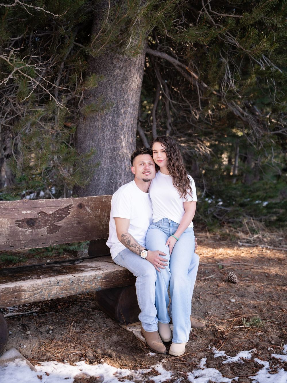 A couple sits together on a rustic wooden log in a peaceful forest setting.