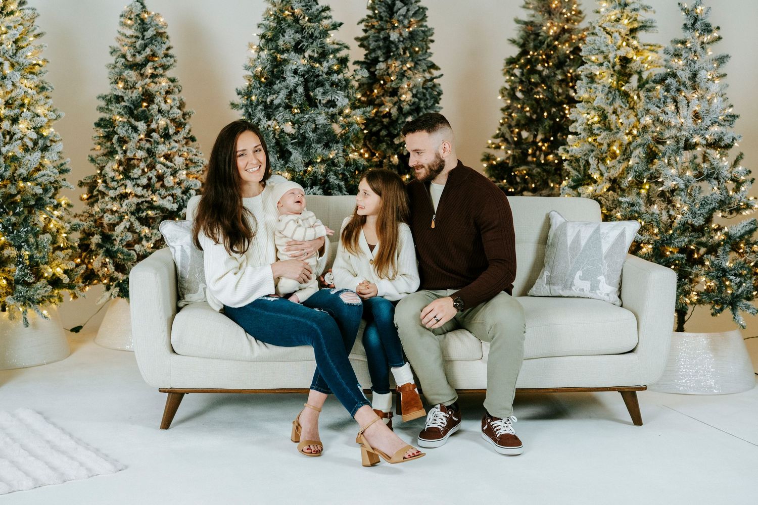 A family sits together on a white couch with multiple decorated Christmas trees glowing in the background.