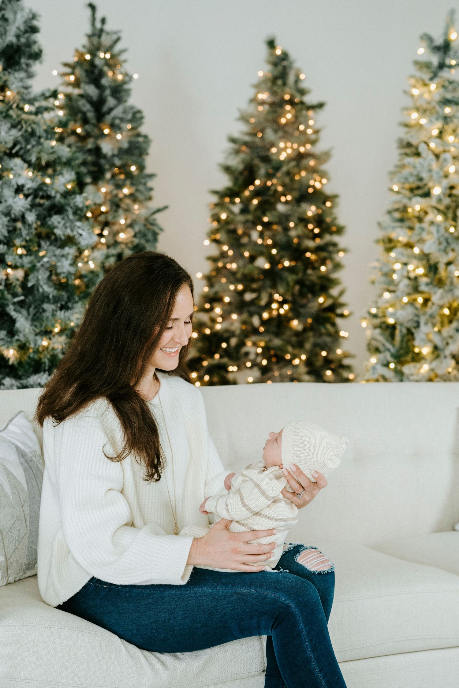 A cozy winter scene with a white couch and illuminated Christmas trees creating a warm holiday atmosphere.