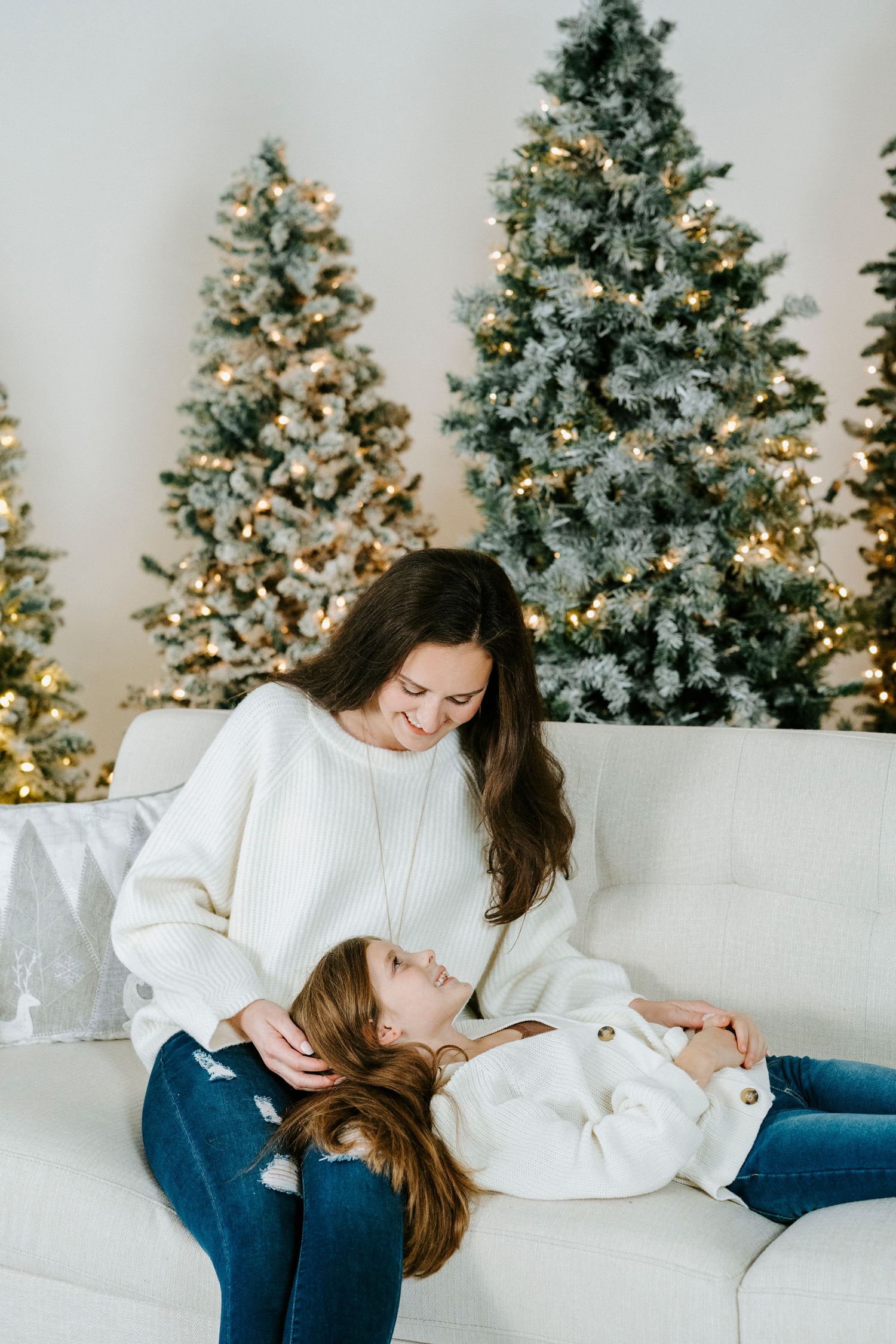 Two people share a cozy moment on a white couch with illuminated Christmas trees in the background.