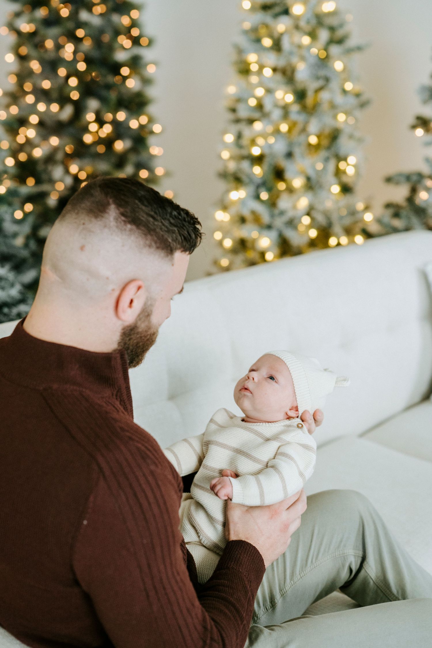 A heartwarming moment between parent and baby against a backdrop of glowing Christmas trees and soft lighting.