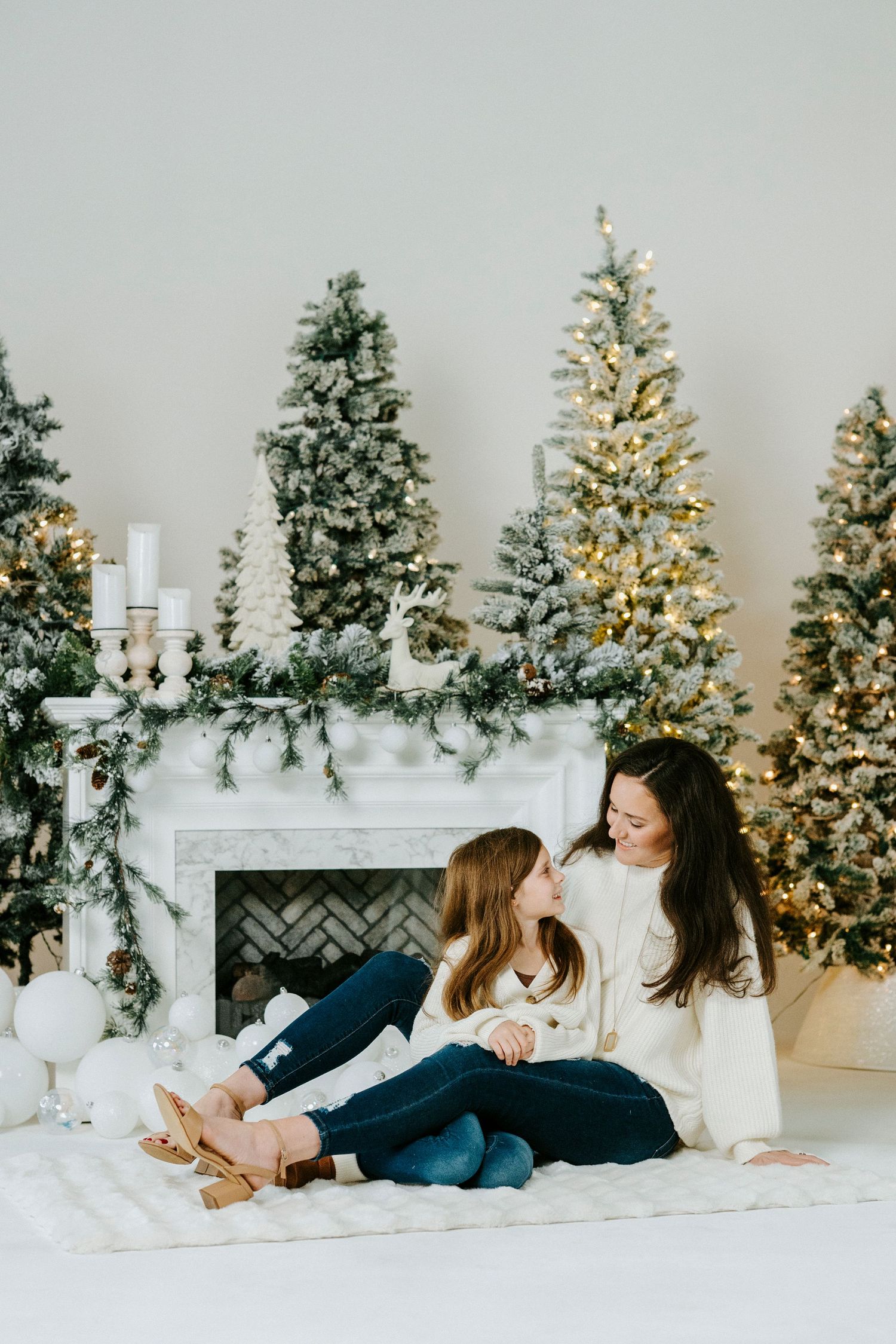 Intimate holiday photo session with decorated Christmas trees and white mantel display in background.