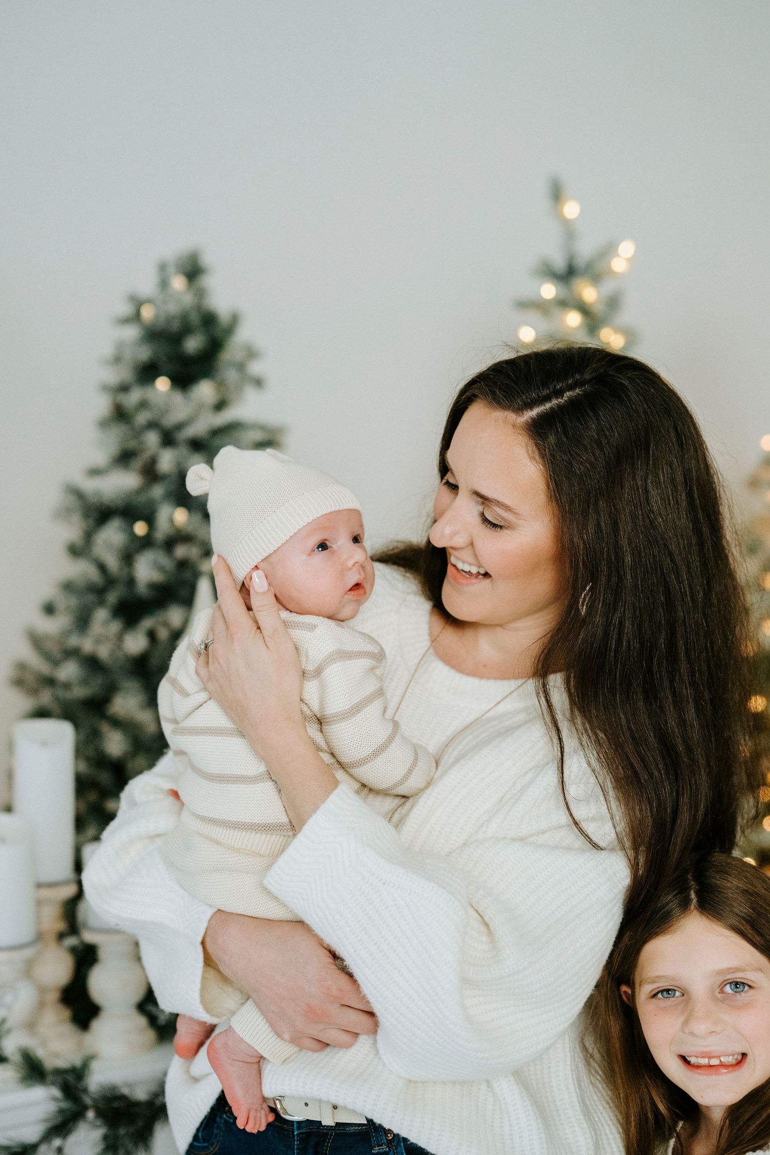 A heartwarming holiday portrait in front of decorated Christmas trees with white winter outfits.