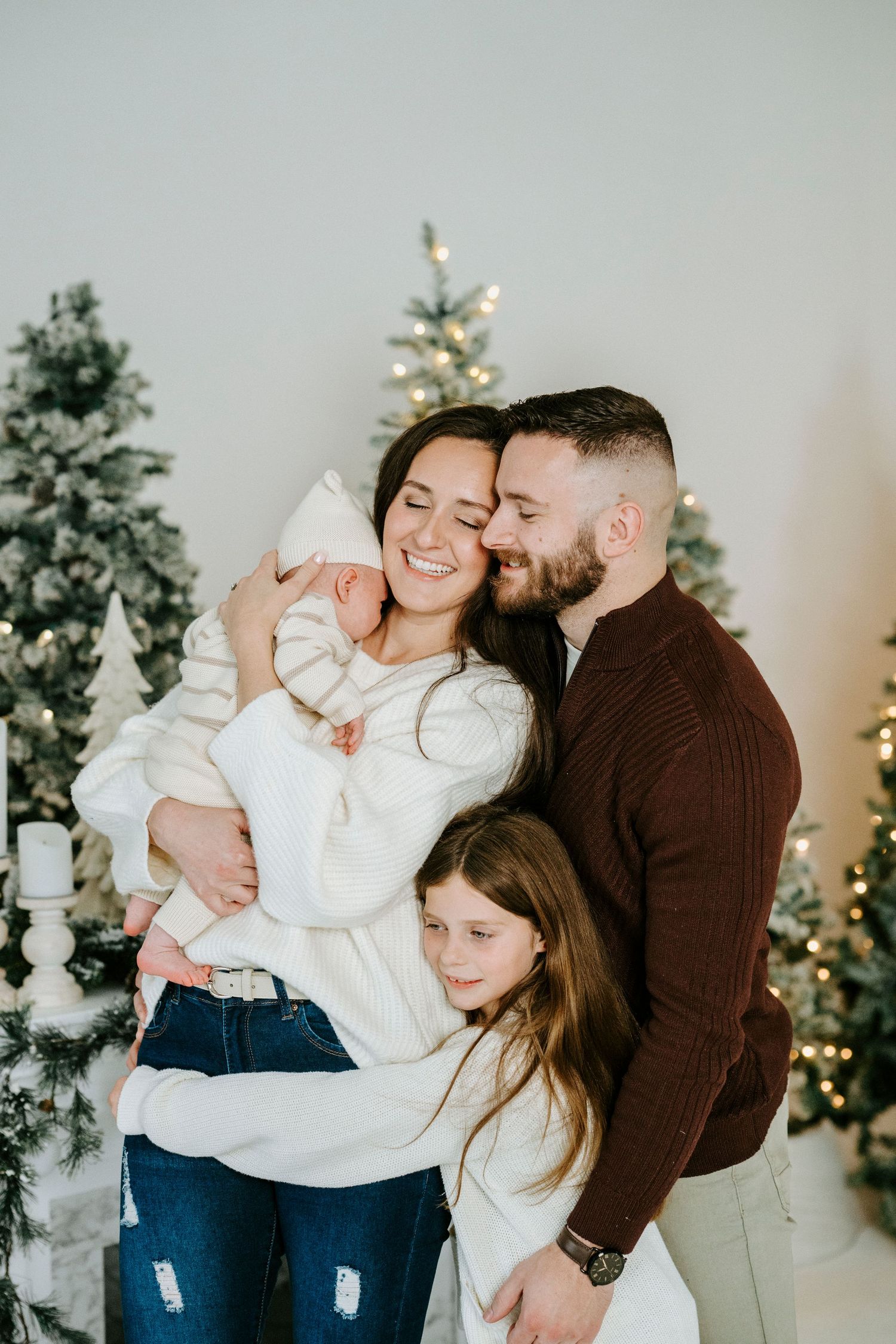 A family shares tender moments together in front of decorated Christmas trees with twinkling lights in the background.