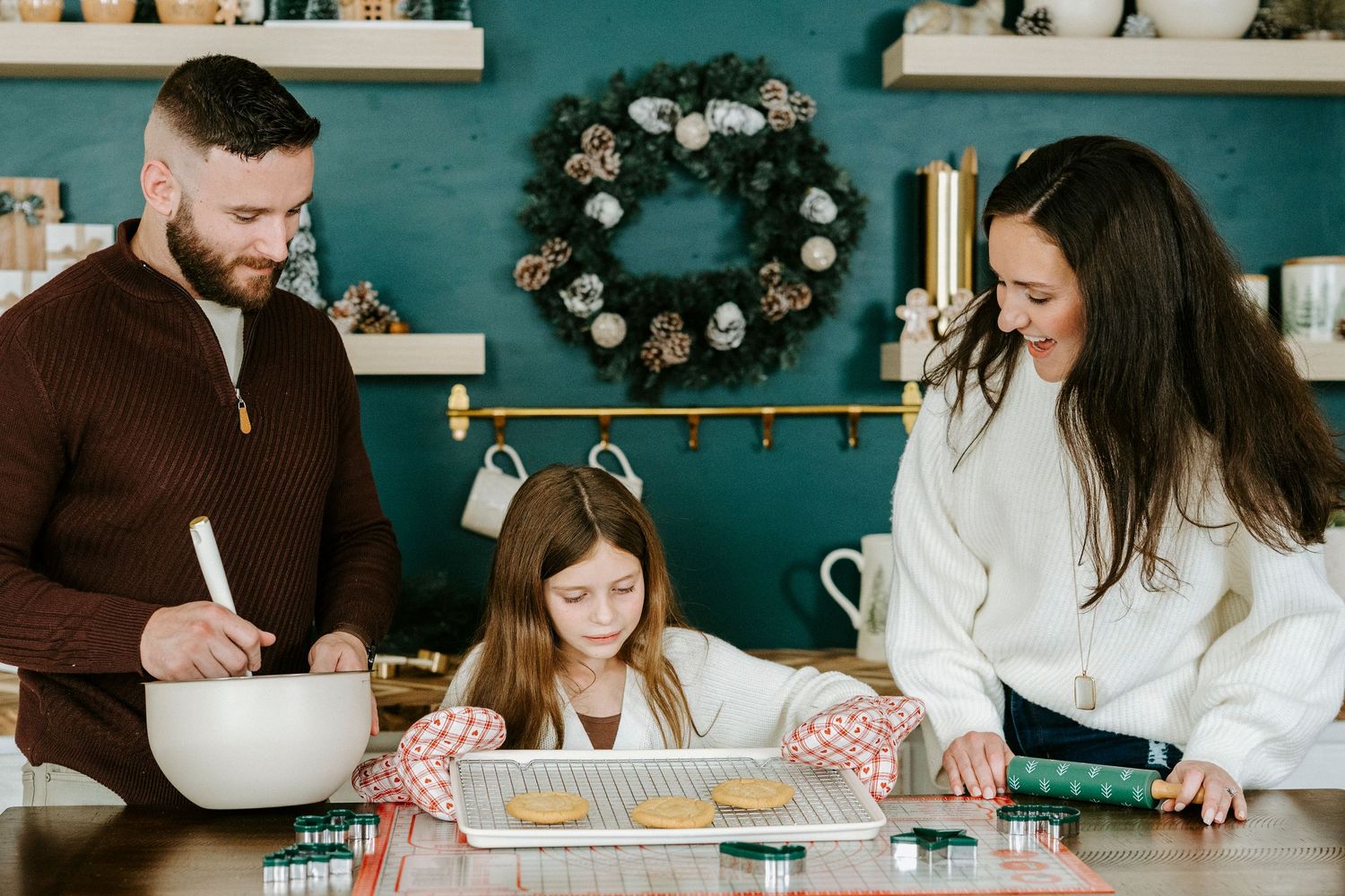 Family gathers around a rustic wooden table working on a craft project together with supplies spread out.