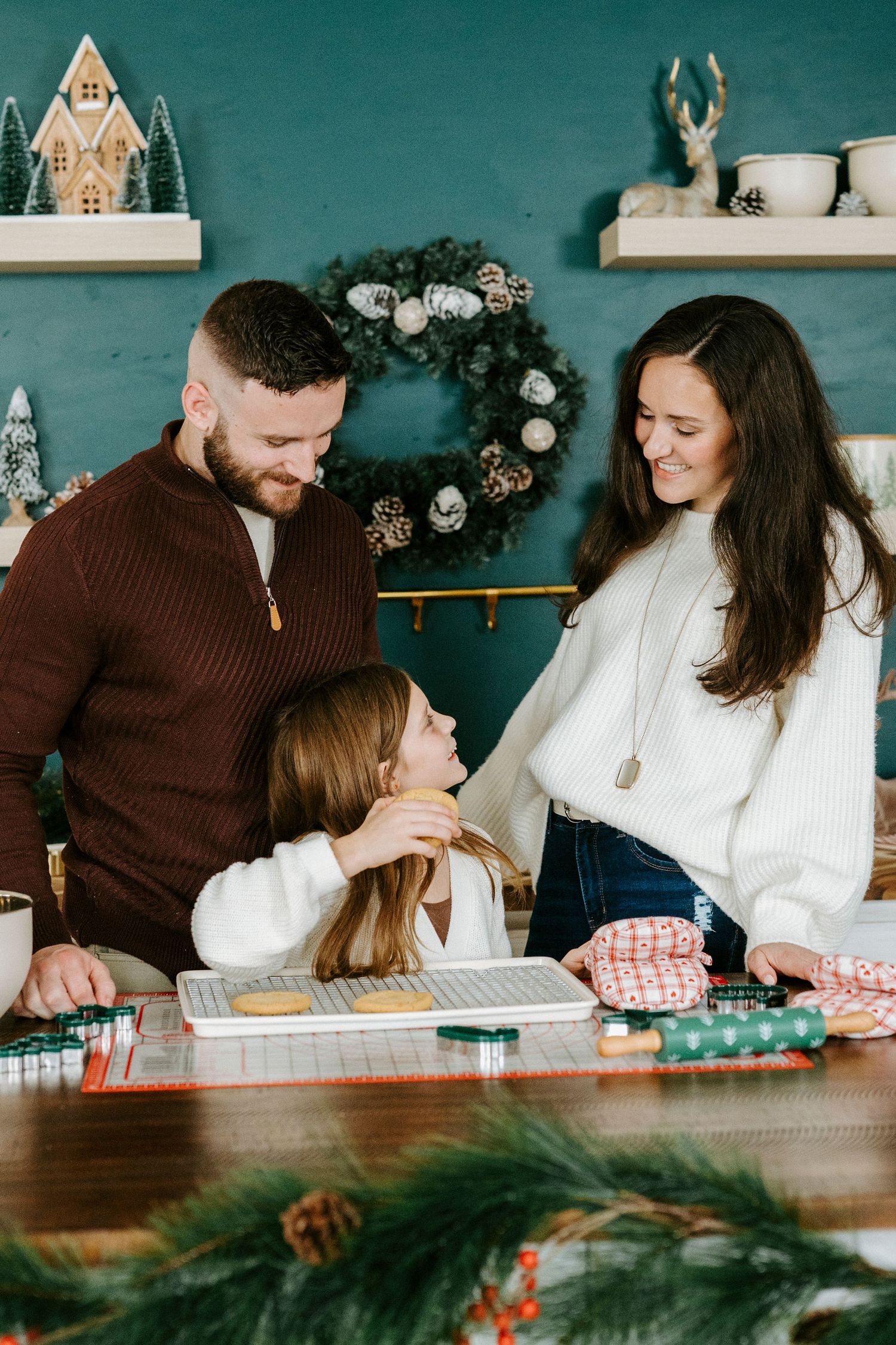 Family shares intimate moments together at a rustic dining table with teal walls and holiday decorations.