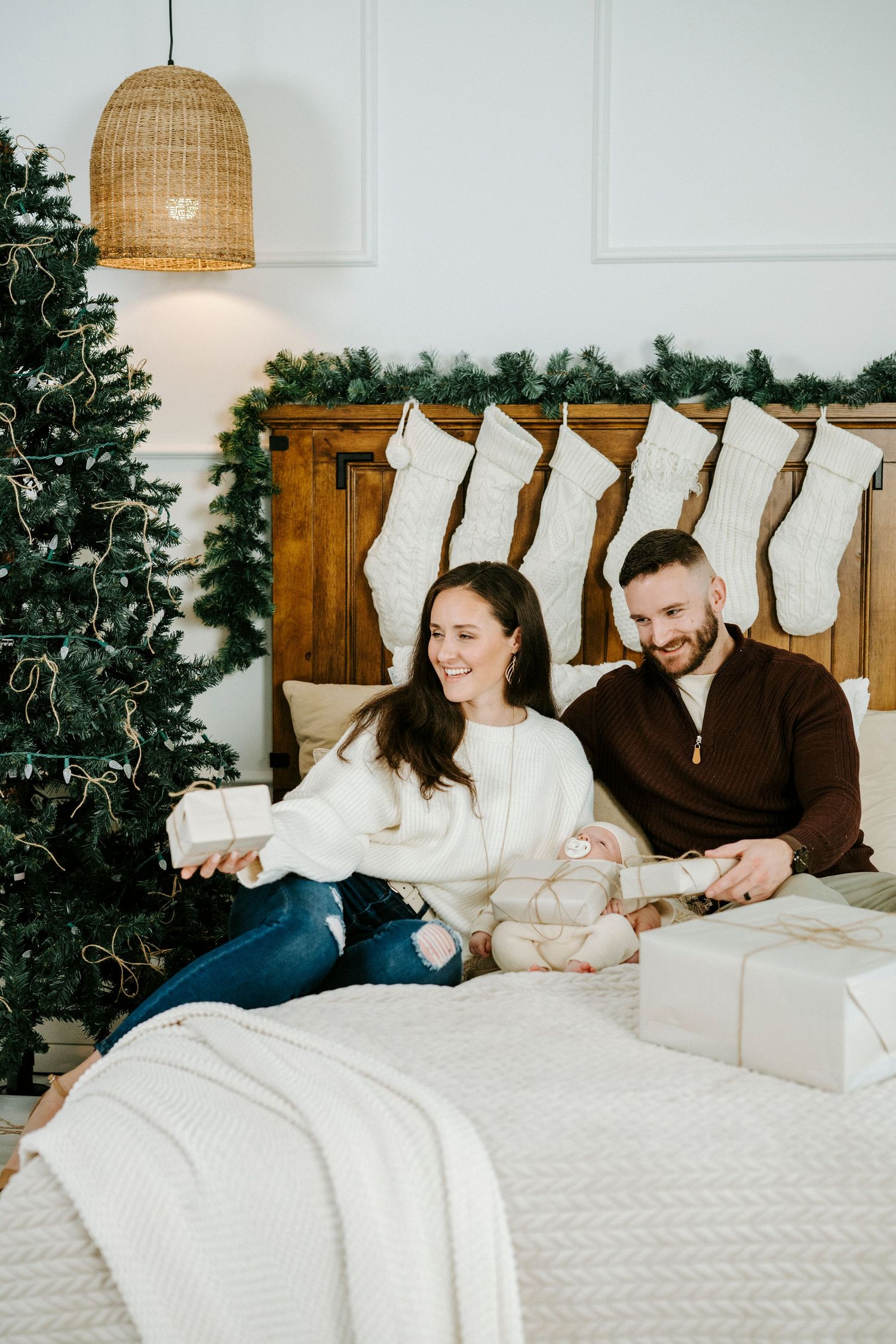 Family relaxing on white bed with Christmas stockings and holiday decor visible in background.