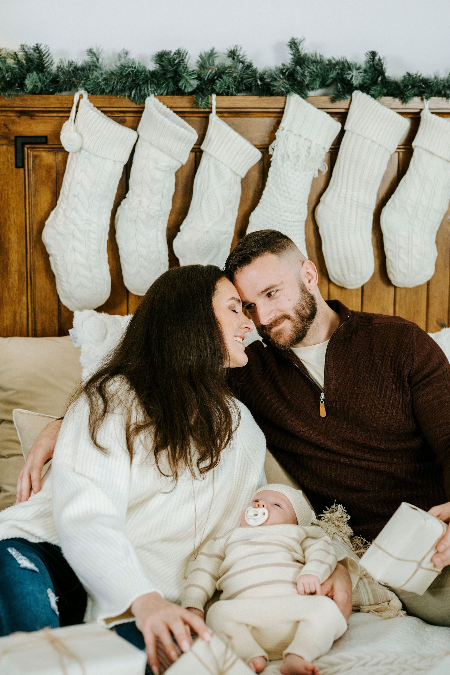 White stockings hang on a wooden wall as a family shares an intimate moment on a couch.