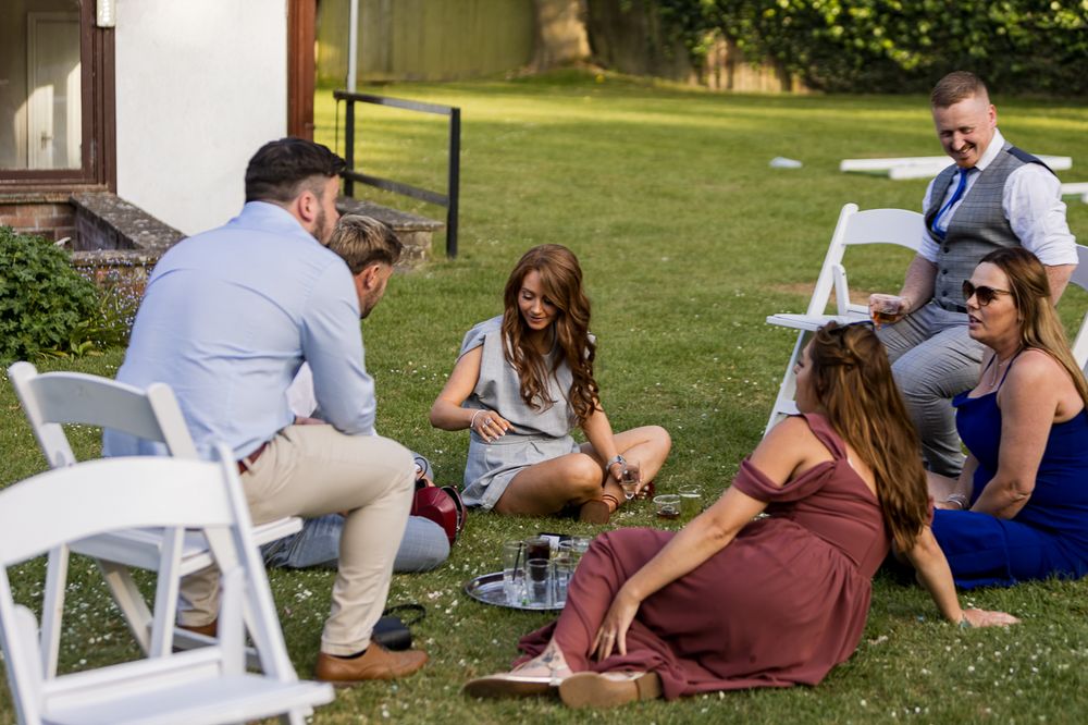 Wedding guests relaxing on white chairs on a lawn during an outdoor reception.