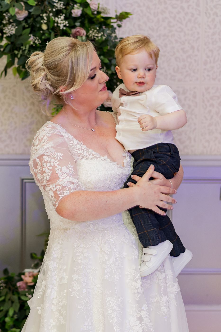 A bride in an elegant lace dress poses near floral decorations during the wedding reception.