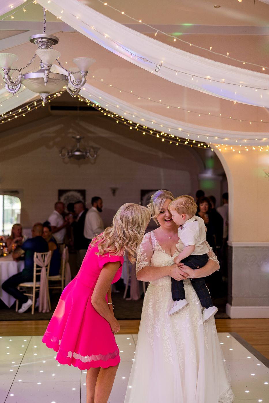 Wedding guests interact on a dance floor decorated with twinkling lights overhead.