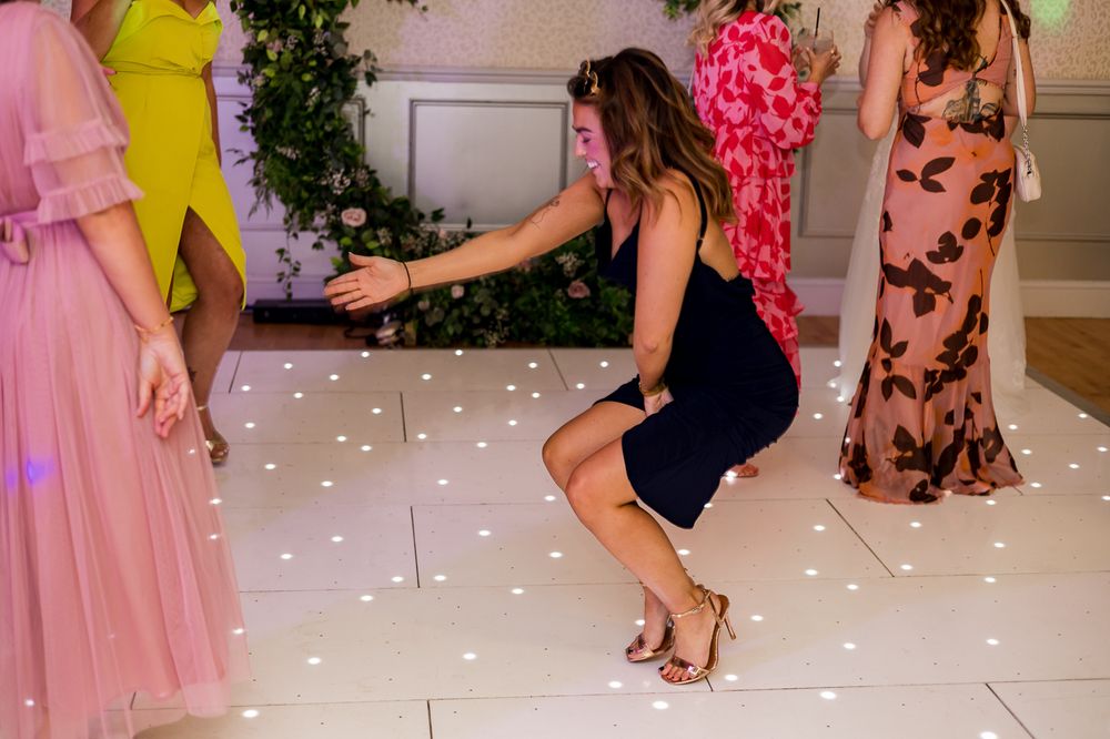 Wedding guest in a navy dress dances energetically on an illuminated white dance floor.